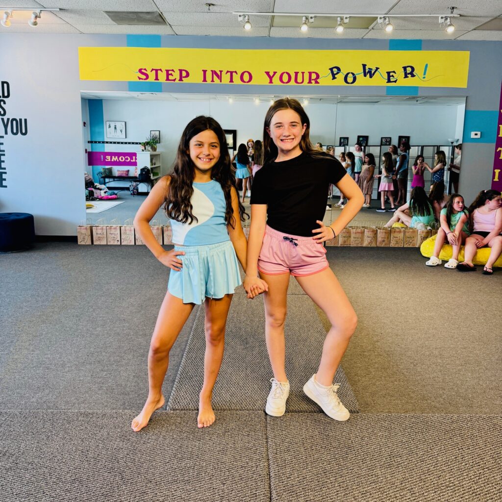 Two girls looking happy and confident at Fearless Focus under a sign that says "Step Into Your Power!"