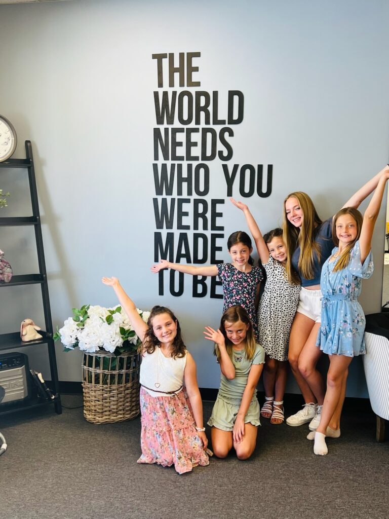 A group of girls at Fearless Focus posing in front of a sign that say the world needs who you were made to be.