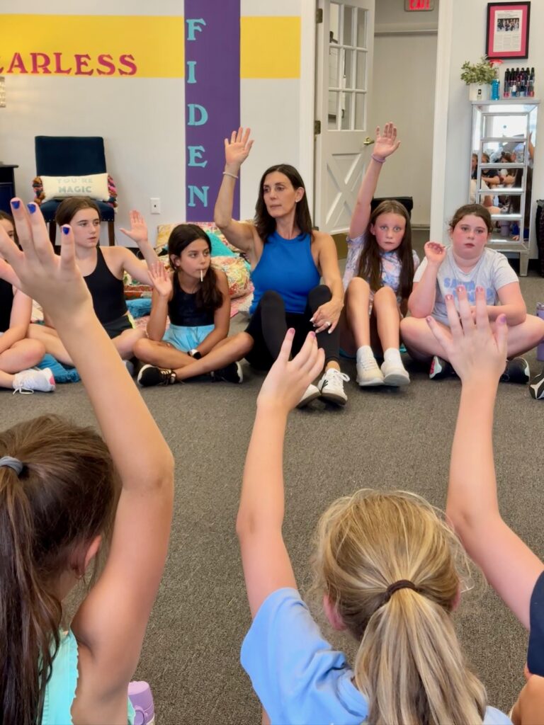Maria and girls at Fearless Focus in a discussion circle raising hands to participate and give their thoughts and opinions. 